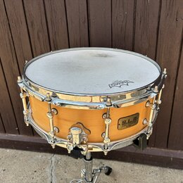 Dřevěný snare drum s přírodním povrchem a chromovaným kováním. Na blaně je viditelné logo REMO a na korpusu štítek s nápisem B.L.A. Custom Line Produ…