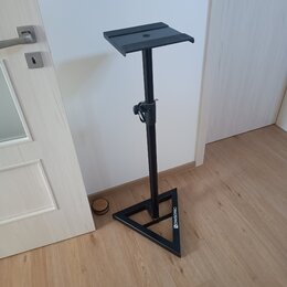 Černý kovový stojan s trojúhelníkovou základnou a plochou horní deskou. Na jedné z hran základny je bílý nápis NOWSONIC. Povrch stojanu vykazuje mírn…