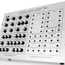 Bílý analogový syntetizátor v kovovém šasi s nápisem telemark na horní hraně. Přední panel obsahuje řadu potenciometrů, přepínačů a zapojovacích kone…