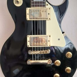Černá elektrická kytara s typickým tvarem singlecut a krémovým pickguardem. Má dva humbuckery se zlatými kryty, zlatý kobylník a čtyři zlaté ovládací…