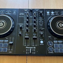 Černý DJ kontrolér s dvěma jog-koly a centrálním mixážním sekcí. Na přístroji je bílý nápis Pioneer DJ a modelové označení DDJ-400 s doplňkem rekordb…