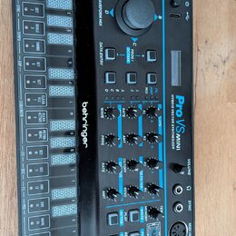 Černý hybridní syntetizátor s modrými detaily a nápisem Pro VS MINI HYBRID VECTOR SYNTHESIZER. Na levé straně je umístěno logo behringer a blok tlačí…