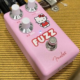 Růžový efekt pedál s nápisem FUZZ a obrázkem postavy Hello Kitty. Na horní části jsou tři bílé ovládací knoflíky s popisky ファズ FUZZ, 音色 TONE a 音量 LEV…