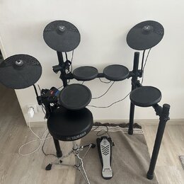 Elektronická bicí souprava v černé barvě s černým rámem. Na sedáku je bílé logo a nápis YAMAHA. Souprava obsahuje několik padů, tři činely a pedál s…