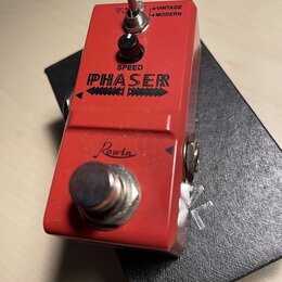 Červený efekt pedál s nápisem PHASER a značkou Rowin. Na horní straně se nachází černý ovládací knoflík s popiskem SPEED a přepínač s nápisy VINTAGE…
