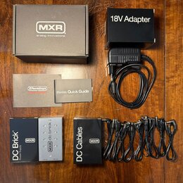 Sada napájecího zdroje pro efekt pedály. Obsahuje černý adaptér s nápisem 18V Adapter, napájecí jednotku DC Brick Power Supply značky MXR a sadu čern…