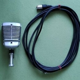 Stříbrný mikrofon v retro stylu s žebrovaným povrchem a kovovým stojankem. K mikrofonu patří černý kabel s konektorem. Povrch mikrofonu vykazuje drob…