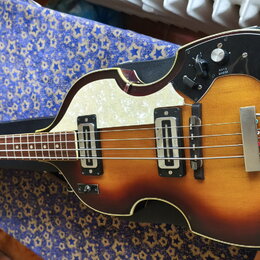 Polodupatá elektrická basová kytara s trupem ve tvaru houslí a barevným přechodem od žluté k tmavě hnědé. Na těle je bílý perleťový pickguard a černý…