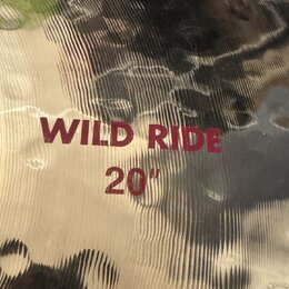 Detailní záběr na povrch mosazného činele s výraznou rýhovanou strukturou a kovem v kmitavém provedení. Na povrchu je červeným nápisem uvedeno WILD R…