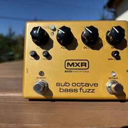 Zlatý efekt pedál s nápisy MXR a BASS INNOVATIONS. Na horní straně jsou čtyři černé oválné knoflíky s popisky GAIN, FUZZ, OCTAVE a DRY. Ve spodní čás…