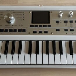Bílá klávesová syntezátor s nápisem KORG microKORG synthesizer vocoder. Přístroj má v horní části ovládací panel s několika otočnými knoflíky, tlačít…