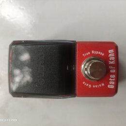 Červený efekt pedál s černým plastovým krytem v levé části. Na červeném povrchu je bílý nápis „Gate of Kahn“ a u spínače texty „True Bypass“ a „Noise…