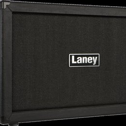 Černý kytarový kombozesilovač nebo box s texturovaným povrchem a látkovou maskou. Uprostřed masky je bílo-černý obdélníkový štítek s nápisem Laney. N…