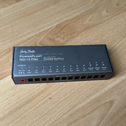 Černý napájecí adaptér s nápisy Harley Benton, PowerPlant ISO-12 Pro a ISOLATED OUTPUT POWER SUPPLY. Zařízení má v horní části řadu modrých kontrolní…