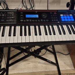 Černý digitální klavír s bílými a černými klávesami, umístěný na černém X-stojanu. Na pravé straně panelu je bílý nápis Roland Juno-DS a sekce PHRASE…