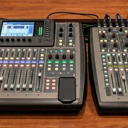 Dvě digitální mixovací konzole černé barvy umístěné vedle sebe na dřevěném povrchu. Na levé konzoli je v horní části viditelné logo a nápis X32. Obě…