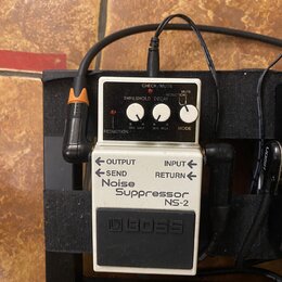 Bílý efekt pedál značky BOSS s nápisem Noise Suppressor NS-2. Zařízení má tři ovládací knoflíky s popisky REDUCTION, THRESHOLD a DECAY, přepínač MODE…