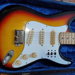 Elektrická kytara s trupem v barevném přechodu od žluté přes oranžovou k červené a černé. Nástroj má bílý pickguard, tři jednoduché snímače a tři ovl…