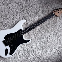 Bílá elektrická kytara s černým pickguardem a hmatníkem z tmavého dřeva. Na hlavě je viditelné logo „Fender“ a nápis „STRATOCASTER“. Nástroj má jeden…