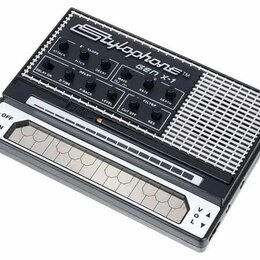 Černý přenosný syntetizátor s bílým nápisem Stylophone TM GEN X-1. Horní panel obsahuje řadu ovládacích knoflíků s popisky jako ATTACK, PITCH, DECAY,…