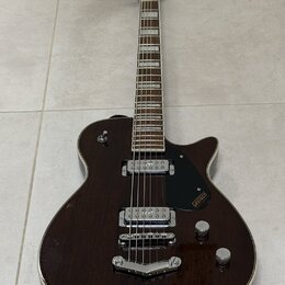 Tmavně hnědá elektrická kytara s polodupovým tělem a bílým lemováním. Na černém plechtraci je viditelné logo GRETSCH a nápis Broadkaster. Nástroj má…