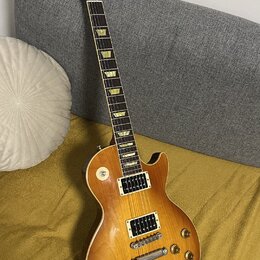 Elektrická kytara s trupem v žlutě-hnědém sunburst provedení a tmavým hnedým hmatníkem s trapezoidními vložkami. Na hlavě je bílý nápis Gibson. Nástr…