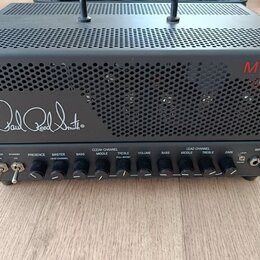 Černý kytarový zesilovač s perforovaným kovovým šasi. Na přední straně je bílý nápis Paul Reed Smith® a v pravém horním rohu červený nápis MT15. Před…