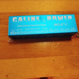 Modrý obdélníkový napájecí adaptér s nápisy CALINE POWER, ISOLATED PROTECTION a CP-8. Na horní straně jsou umístěny konektory s popisky DC 18V IN, DC…