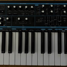 Černý analogový syntetizátor s bílými a černými klávesami. Na levé straně je nápis novation BASS STATION 2 Analogue synthesizer. Přední panel obsahuj…