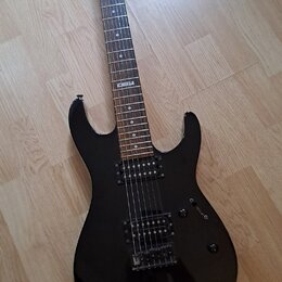 Černá elektrická kytara s tmavým hnedým hmatníkem a dvěma humbuckery. Na hmatníku je viditelný bílý štítek s nápisem "No 107". Na hlavě krku je bílé…