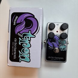 Fotografie zobrazuje kytarový efekt a jeho originální krabici. Na pedálu i na krabici je nápis „electro-harmonix NEW YORK CITY, USA“ a velký grafický…