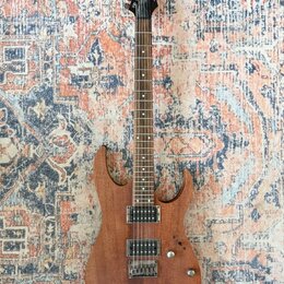 Elektrická kytara s hnědým dřevěným povrchem těla a hnedou hmatníkem. Na hlavě je bílý nápis Ibanez. Nástroj má dva humbuckery, jeden ovládací knoflí…