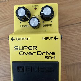 Žlutý efekt pedál s černým spínacím tlačítkem. Na horní části jsou tři ovládací knoflíky s popisky LEVEL, TONE a DRIVE a kontrolka s nápisem CHECK. N…