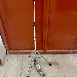 Stříbrný kovový stativ s černými plastovými prvky a trojnožkou. Na spodní části je připevněn šedý plastový pedalboard. Povrch stativu vykazuje známky…