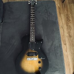 Elektrická kytara s trupem v černo-žlutém sunburst provedení a černým pickguardem. Na hlavě hmatníku je viditelné logo Vintage. Nástroj má dva snímač…