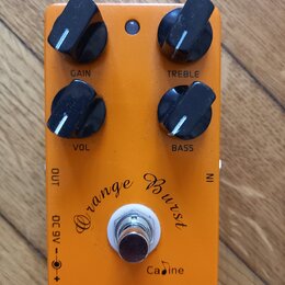 Oranžový efekt pedál s nápisy Orange Burst, Cadine a OVERDRIVE. Pedál má čtyři černé ovládací knoflíky s popisky GAIN, TREBLE, VOL a BASS. V dolní čá…