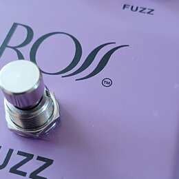 Fialový efekt pedál s nápisem BOSS a symbolem ™. Na horní straně jsou dva černé oválné ovladače s popisky LEVEL a FUZZ. V dolní části je vidět část n…