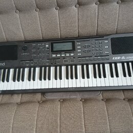 Černý digitální klavír s bílými a černými klávesami. Na levé straně je bílý nápis Roland a vpravo nápis EXR-5s INTERACTIVE ARRANGER. Horní panel obsa…