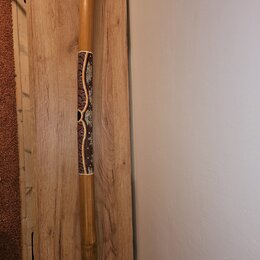 Dřevěný didgeridoo v přirozené hnědé barvě. Střed nástroje je zdobený ornamentálním vzorem v červených, bílých a žlutých odstínech. Na nástroji nejso…
