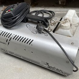 Stříbrný kouřový stroj z kovu s bílou plastovou nádržou na tekutinu. Na přístroji jsou nápisy „Antari“, „Z-1200 SMOKE FOGGER“ a „Z 1200 series“. Povr…