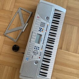 Světle šedý elektronický klavír s plastovým korpusem a bílo-černými klávesami. Na přístroji jsou viditelné nápisy „128 TONE“ a „128 VOICE“, uprostřed…