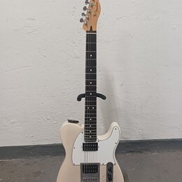 Elektrická kytara s bílým trupem, bílým pickguardem a hnědým hmatníkem. Na hlavě je viditelné logo Fender. Nástroj má dva snímače, jeden v pozici kob…