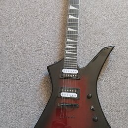 Elektrická kytara s ostře hranatým korpusem v černo-červeném přechodovém lakování. Na hlavě hmatníku je bílý nápis Cort. Nástroj má dva humbuckery, d…