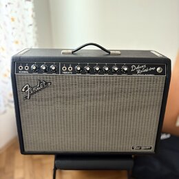 Černý kytarový kombozesilovač s šedou textilní maskou. Na horním ovládacím panelu jsou nápisy NORMAL, VIBRATO a Deluxe Reverb Amp, dále označení VOLU…