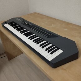 Šedý syntetizátor s klávesnicí položený na světlém dřevěném stole. Na levé straně horního panelu je bílý nápis Roland JX-8P. Povrch přístroje vypadá…