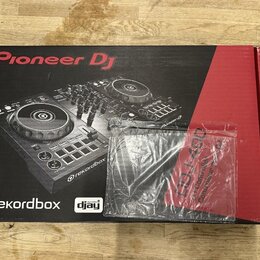 Kartonová krabice s obrázkem DJ kontroléru v černém a červeném provedení. Na krabici jsou nápisy Pioneer DJ, rekordbox a djay. Před krabicí leží průh…