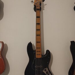 Černá elektrická basová kytara s černým pickguardem a hnedým hmatníkem. Na hlavě je viditelný nápis Fender JAZZ BASS. Nástroj vykazuje běžné známky p…