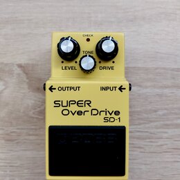 Žlutý efekt pedál s nápisy SUPER OverDrive a SD-1. Na horní části jsou tři stříbrné ovládací knoflíky s popisky LEVEL, TONE a DRIVE a červená kontrol…