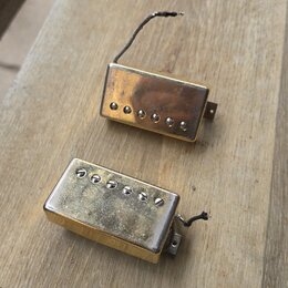 Dvě elektrické kytarové snímače typu humbucker v pozlaceném provedení. Snímač v horní části má hladký kryt s viditelnými šrouby, spodní snímač má kry…