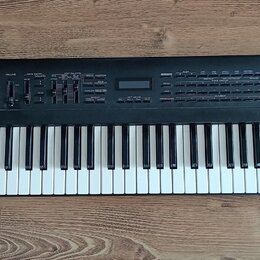 Černý digitální klávesový nástroj s bílými a černými klávesami. Na pravé straně ovládacího panelu je bílý nápis Roland JV-50 EXPANDABLE SYNTHESIZER.…
